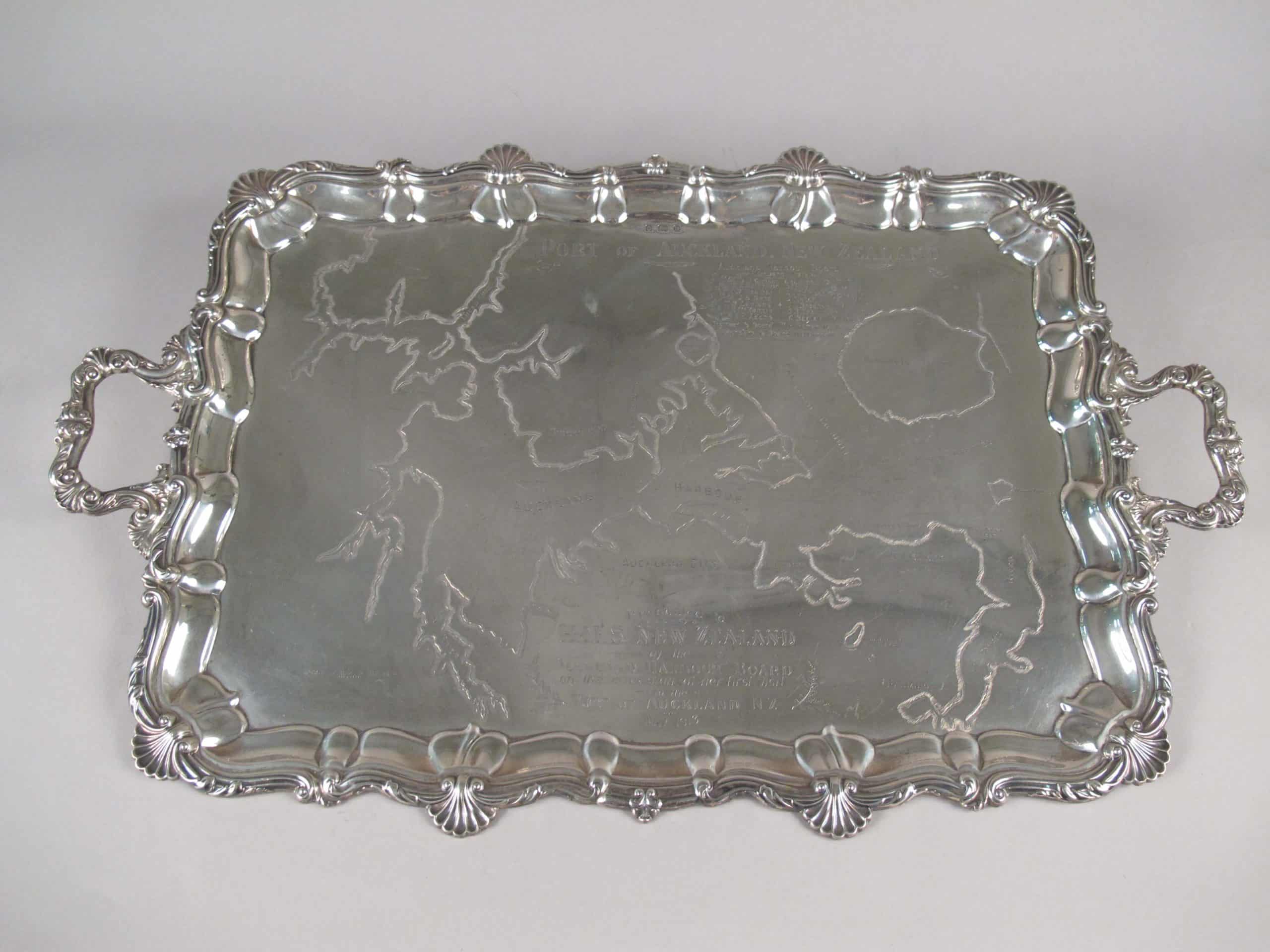 Silver tray with an engraved map of Auckland Harbour. Part of an eight piece silver tea service that includes kettle, salamander (stand), sugar bowl, cream jug, two engraved salvers and an engraved greenstone tablet. These were presented to HMS New Zealand by the Auckland Harbour Board. The inscription reads: ‘Presented to HMS NEW ZEALAND by the Auckland Harbour Board on the occasion of her visit to the Port of Auckland NZ May 1913’.