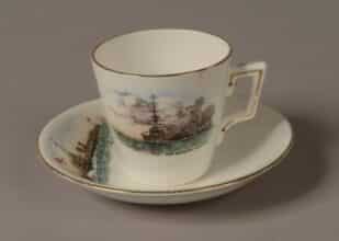Demi Tasse white porcelain coffee cup and saucer with a gold rim around the top. Front of cup is decorated with a picture of a World War One battleship firing a broadside with painted words: ‘H.M Battleship in action’. Top of saucer is decorated with a picture of a World War One torpedo boat with a white ensign at the jack. Words on the saucer read: ‘H.M Torpedo Boat’.